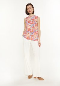 Top senza maniche floreale in colori vivaci con scollatura rotonda, abbinato a pantaloni bianchi a gamba larga e scarpe con tacco a blocco marroni.