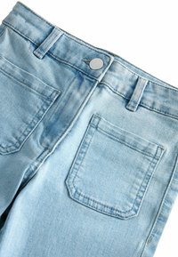 Jeans en denim bleu clair avec taille haute, cinq poches et fermeture à bouton en argent. Texture lisse et finition légèrement délavée.