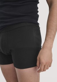 Zwarte boxershorts, gemaakt van een gladde, rekbare stof, met een elastische tailleband. De pasvorm is strak en toont een schoon en eenvoudig ontwerp.