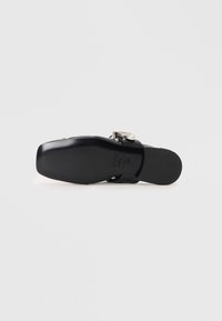 Black leather sandal with a rounded toe, a flat sole, and a decorative silver buckle on the strap. Smooth texture, minimal design.