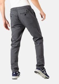 Pantalones gris ajustados con cintura elástica, dos bolsillos traseros con botones y una textura sutil; combinados con zapatillas deportivas en color azul marino.
