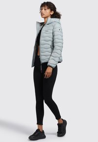 Lyseblå pufferjakke med quiltet tekstur, hætte og lynlås. Båret over en sort top og stramme sorte bukser med sorte sneakers.