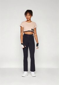 Vaaleanpunainen lyhyt yläosa, jossa "NE"-teksti, mustat korkeavyötäröiset urheiluhousut ja valkoiset lenkkarit; käsineissä kumipäällysteiset otteet; sileä kangas.