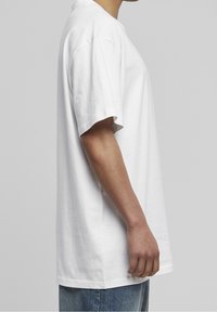 Bílý oversized bavlněný tričko s krátkým rukávem, kulatým výstřihem a volným střihem. Hladká textura a minimalistický design bez vzorů.