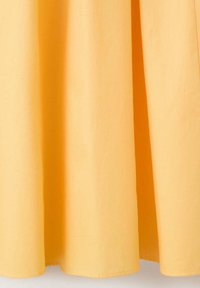 Rideau en tissu jaune suspendu avec des plis doux et des détails subtils d'ombre visibles près du bord inférieur.