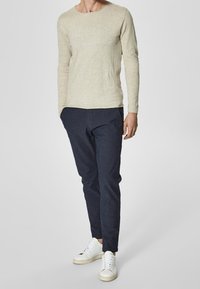 Light beige long-sleeve top, navy slim-fit pants, and white sneakers. Soft texture, casual design, and fitted silhouette.