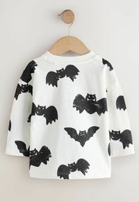 Camisa blanca de manga larga con un patrón de murciélagos negros repetido, hecha de suave tela de algodón, con cuello redondo y puños acanalados.