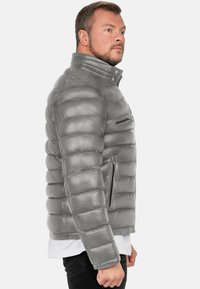 Grijze leren pufferjack met een hoge kraag, doorgestikte design, ritssluiting op de borstzak en zijzakken, met een gladde textuur.