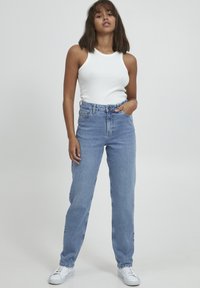 Jeans de mezclilla azul de cintura alta con corte recto, que presentan cinco bolsillos y costuras en contraste, combinados con una blusa sin mangas blanca.