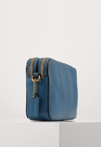 Blue textured leather wallet with gold zippers, featuring a keychain tag detail, displayed against a minimalistic white background.