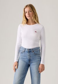 Bílé tričko s dlouhým rukávem s malou červenou nášivkou s logem Levi's, v kombinaci s světle modrými džínami s vysokým pasem. Měkký bavlněný materiál.