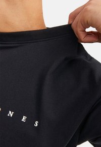 Zwarte katoenen t-shirt met een ronde hals en een relaxte pasvorm, met witte tekst op de borst en een gladde, zachte textuur.