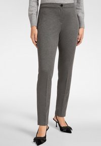 Szare dopasowane spodnie o gładkiej fakturze, slim fit, z zapięciem na guziki w pasie. W połączeniu z czarnymi butami z ozdobnymi kokardkami.