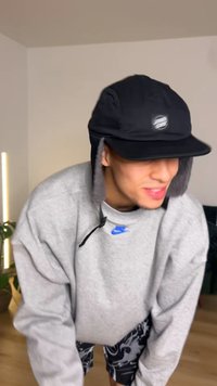 Svart mössa med öronlappar, med en logotyp framtill. Grå sweatshirt, lös passform, med blå Nike-logotyp. Nedre delen visar mönstrade shorts.