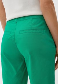 Pantalon vert taille haute en tissu léger avec un léger éclat, équipé de poches arrière et d'une coupe ajustée.