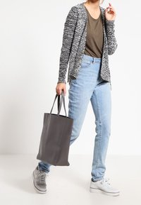 Grå stickad cardigan över en olivgrön topp, tillsammans med ljusblå jeans och en grå toteväska. Modellen bär vita sneakers.