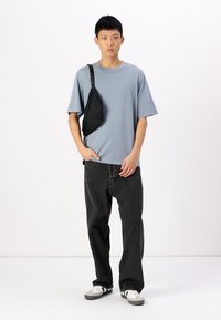 Camiseta de manga corta azul claro, de corte relajado, combinada con jeans anchos negros. Los accesorios incluyen un bolso cruzado negro y zapatillas grises.