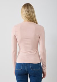 Langärmliges, tailliertes Oberteil aus weichem, dehnbarem Stoff in Hellrose, mit rundem Ausschnitt und nahtlosem Design auf der Rückseite.