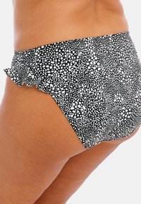 Bas de bikini noir et blanc avec un motif à pois, des bords froncés et un design mi-haut, fabriqué en matière de maillot de bain extensible.