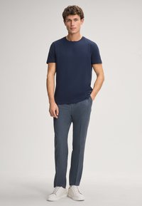 Navy blauwe t-shirt met korte mouwen gecombineerd met gestructureerde grijze broeken en witte sneakers. Eenvoudig ontwerp met een ronde hals en minimale branding.
