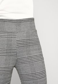 Grå och svart rutiga byxor med en figurnära design, slät tygkonsistens och en bred midjeresår.