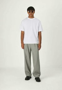 T-shirt branca de manga curta combinada com calças largas cinza claro, com textura suave, usada com sapatos pretos e óculos de sol redondos.