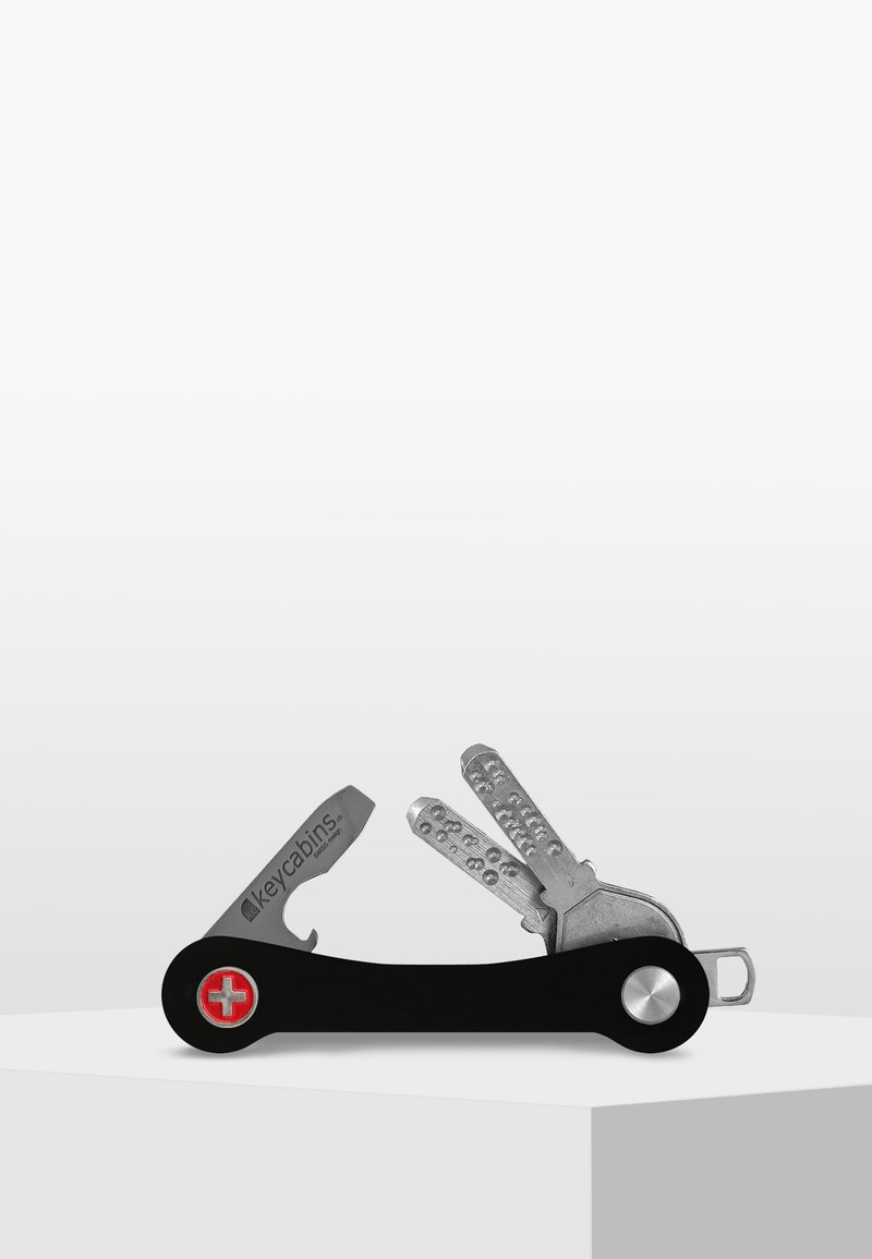 Porte-clés multifonction avec une poignée noire élégante, des outils en acier inoxydable et un emblème suisse rouge. Inclut un espace de rangement pour les clés et des accents en métal.