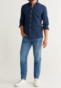 Camicia blu navy con maniche lunghe, jeans azzurri chiari e sneakers bianche. La camicia presenta un motivo sottile e un design con colletto classico.