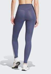 Hoge taille, strakke leggings in donkerblauw met witte zijstrepen; gladde, rekbare stof; gecombineerd met witte sportschoenen.