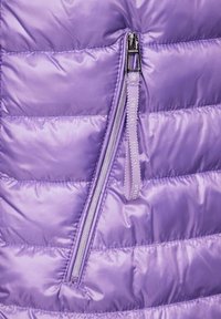 Lila pufferjacka med kviltat mönster, glänsande nylonmaterial och en diagonalt placerad dragkedja med ett logomärkt draghandtag. Slät yta och lättviktig.