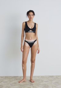 Czarny stanik sportowy Calvin Klein i pasujące majtki bikini. Gładki materiał z logo, z wycięciami na staniku.