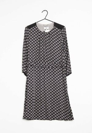 Schwarzes Kleid mit langen Ärmeln, mit hexagonalen Mustern in Weiß und Rosa. Hat einen runden Halsausschnitt und einen Taillengürtel. Glattes Material, hängt an einem Haken.