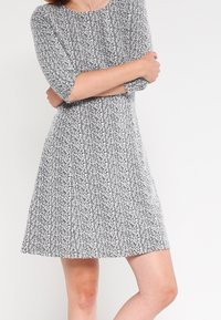 Svartvit mönstrad klänning med rund halsringning och trekvartsärmar, som har en figurnära bodice och en utsvängd kjol.