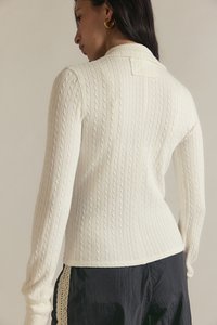 Κρεμ πουλόβερ με ριμπ ύφανση, ψηλό γιακά, μακριά μανίκια και εφαρμοστή γραμμή, με ανάγλυφες λεπτομέρειες πλεξίματος καλωδίου.