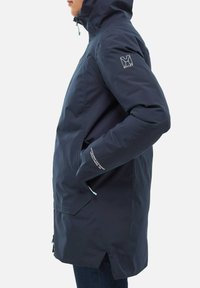 Veste imperméable bleu marine avec capuche, poches zippées et une ventilation zippée dans le dos. Comprend un logo sur la manche et un texte réfléchissant.