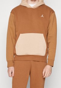 Felpa con cappuccio marrone e beige con tasca a marsupio; presenta un piccolo logo bianco di Jordan sul petto, realizzata in tessuto morbido.