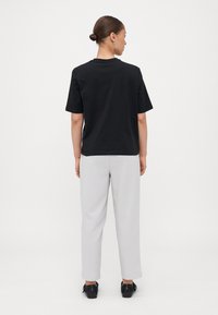 T-shirt en coton noir à manches courtes, assortie à un pantalon gris clair. La tenue présente un design simple et une coupe décontractée. Des chaussures noires complètent le look.
