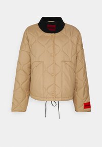 Beige quiltet jakke med sort krave, trykknapper, forlommer og røde HUGO-logo-patch på kraven og ærmegabet.