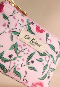 Pungă cu fermoar roz floral de la Cath Kidston, având frunze verzi și flori roz, cu o textură din material și accente din metal auriu.