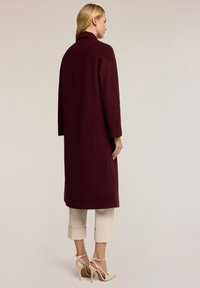 Cappotto in lana borgogna con taglio dritto, maniche lunghe e colletto classico, caratterizzato da una texture liscia e da elementi di design minimi.