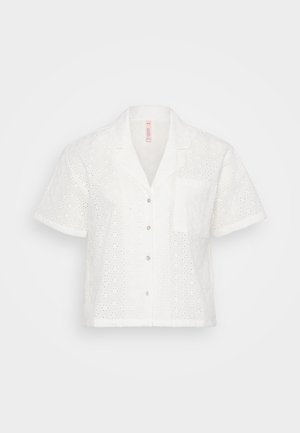 Camisa branca de manga curta com um padrão de broderie anglaise floral, apresentando colarinho em bico, fecho com botões e um único bolso no peito.