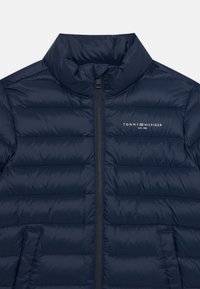 Casaco puffer azul-marinho, design acolchoado, gola alta, fecho frontal com zíper e bolsos laterais. Apresenta um logótipo no lado superior esquerdo.