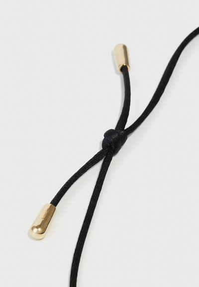 Crni kabel s čvorom, s metalnim zlatnim agletama. Tekstura je glatka i sjajna, u kontrastu s mat završetkom kabela.