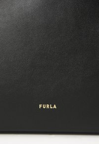 Fekete bőr táska texturált felülettel, arany "FURLA" logóval az alján. Egyszerű és minimalista dizájn.