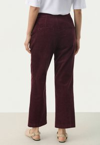 Bordeaux corduroy broek met een recht model, voorzien van twee achterzakken en een subtiele ribbeltextuur. Gecombineerd met een lichte top en sandalen.