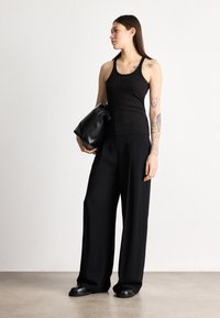 Μαύρο ριμπ αμάνικο τοπ, φαρδιά μαύρη παντελόνα και μαύρη τσάντα ώμου. Λεία υφή, μίνιμαλ σχεδιασμός και άνετη γραμμή. Μοντέλο με τατουάζ.