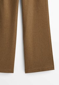 Pantalon marron à jambes larges avec des coutures visibles à l'ourlet, présenté sur fond blanc.