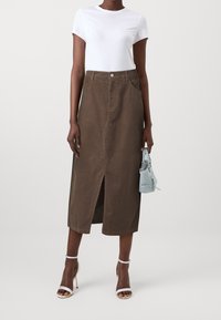 Brown corduroy skirt with a front slit, paired with a fitted white t-shirt and light blue handbag. Features a button at the waist.