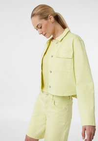 Skórzana kurtka z denimu w kolorze jasnego żółtego oraz dopasowane szorty, z zatrzaskami, dwiema kieszeniami na piersiach i teksturowanym materiałem.