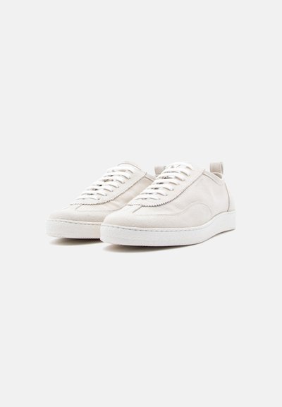 Ζευγάρι εκρού σουέντ αθλητικά παπούτσια με λευκά κορδόνια και λαστιχένιες σόλες, τοποθετημένα δίπλα δίπλα πάνω σε απλό ανοιχτόχρωμο φόντο.